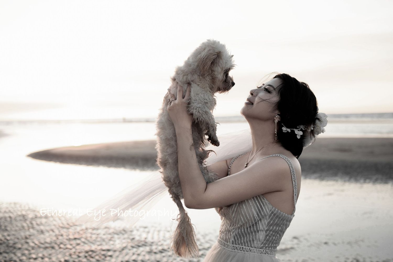 A couple embraces on a serene beach during sunset with soft golden light.