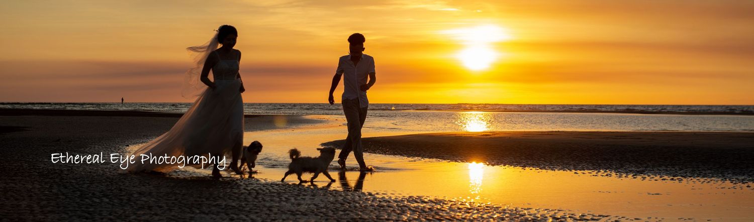 Silhouettes of people walking along a beach at sunset with dramatic orange sky and reflections on the water.