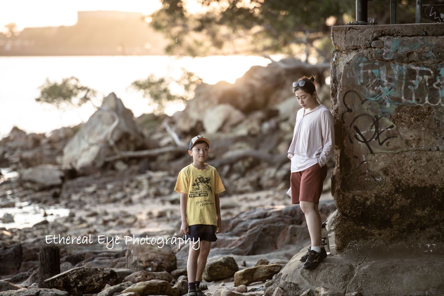 Children playing on rocky coastal terrain during golden hour with trees in the background.