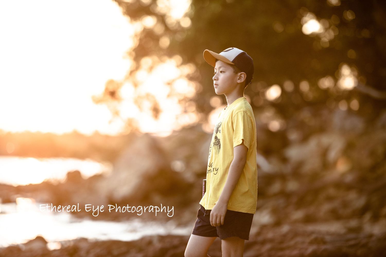 Dreamy backlit scene of people on rocky shore during golden hour.