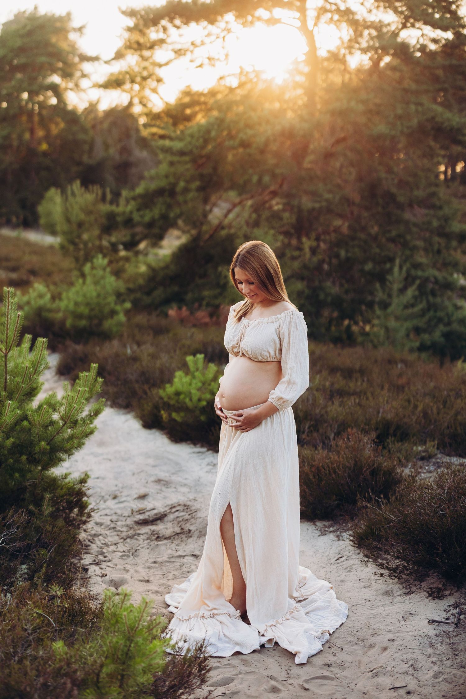 Maternity photoshoot at sunset on a sandy path surrounded by natural vegetation.