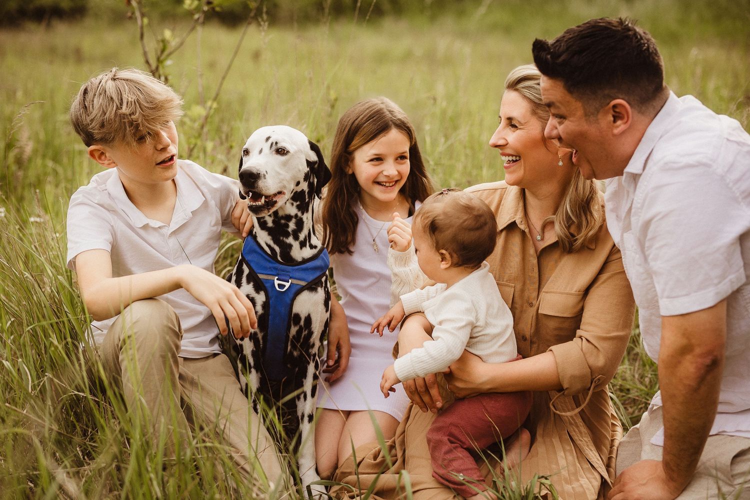 Family enjoying a playful moment together outdoors in a grassy field with their dog.