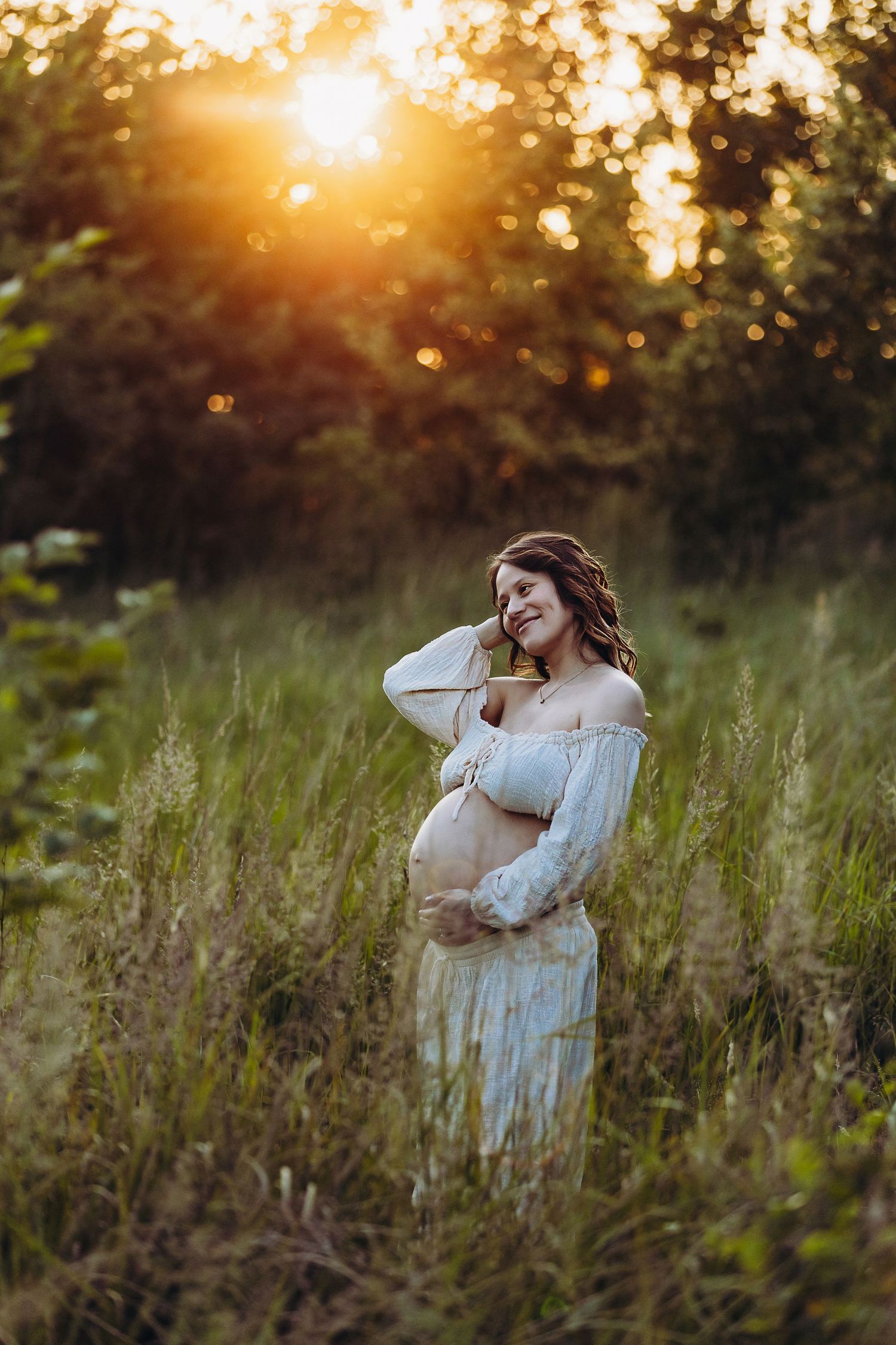 Ethereal maternity portraits in a meadow during golden hour sunset.