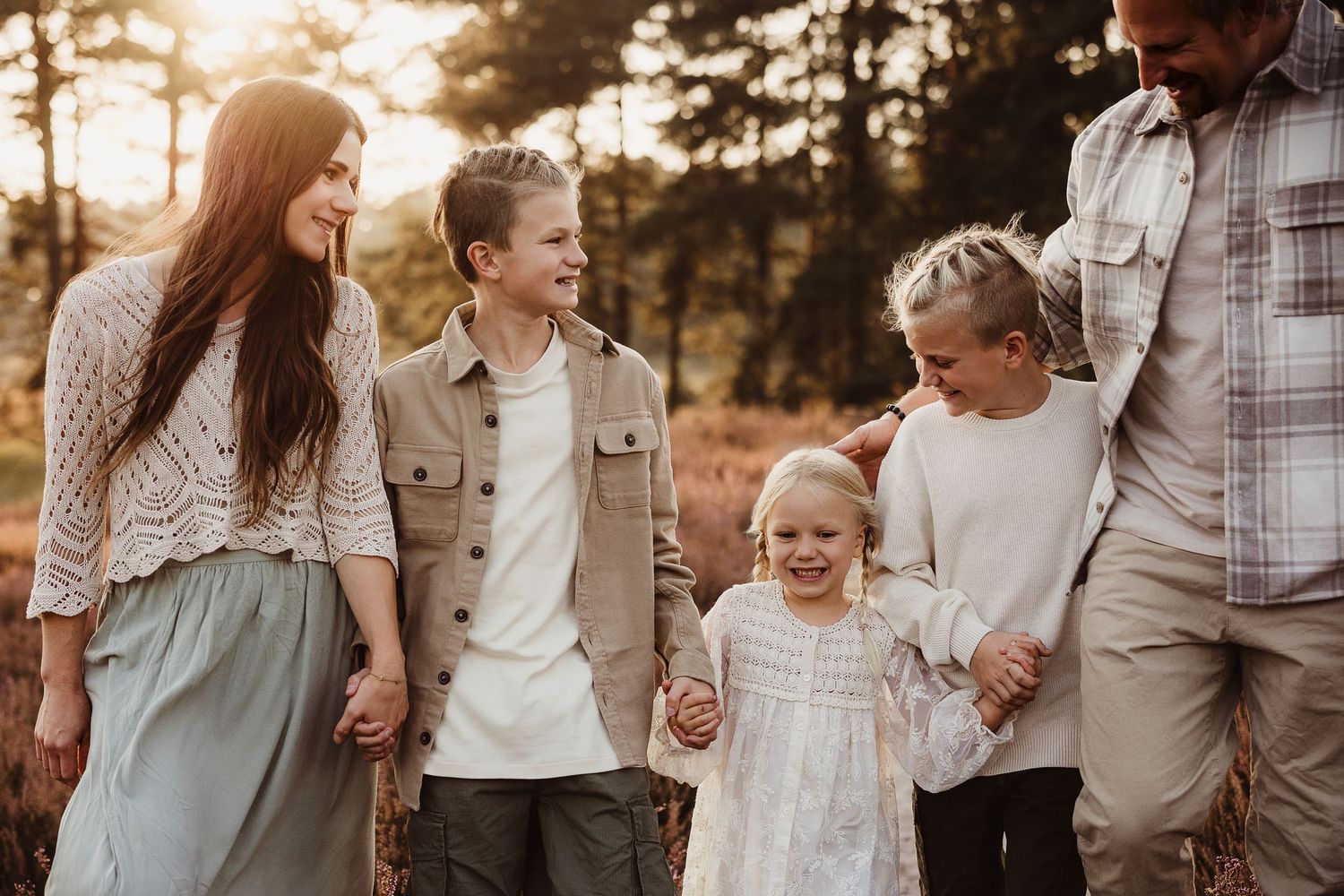 Family walking together in casual neutral outfits during golden hour sunset.