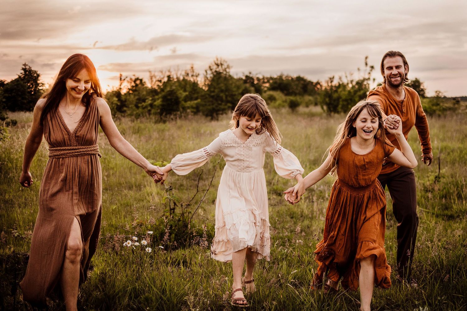 Family members holding hands while walking through a golden field at sunset.