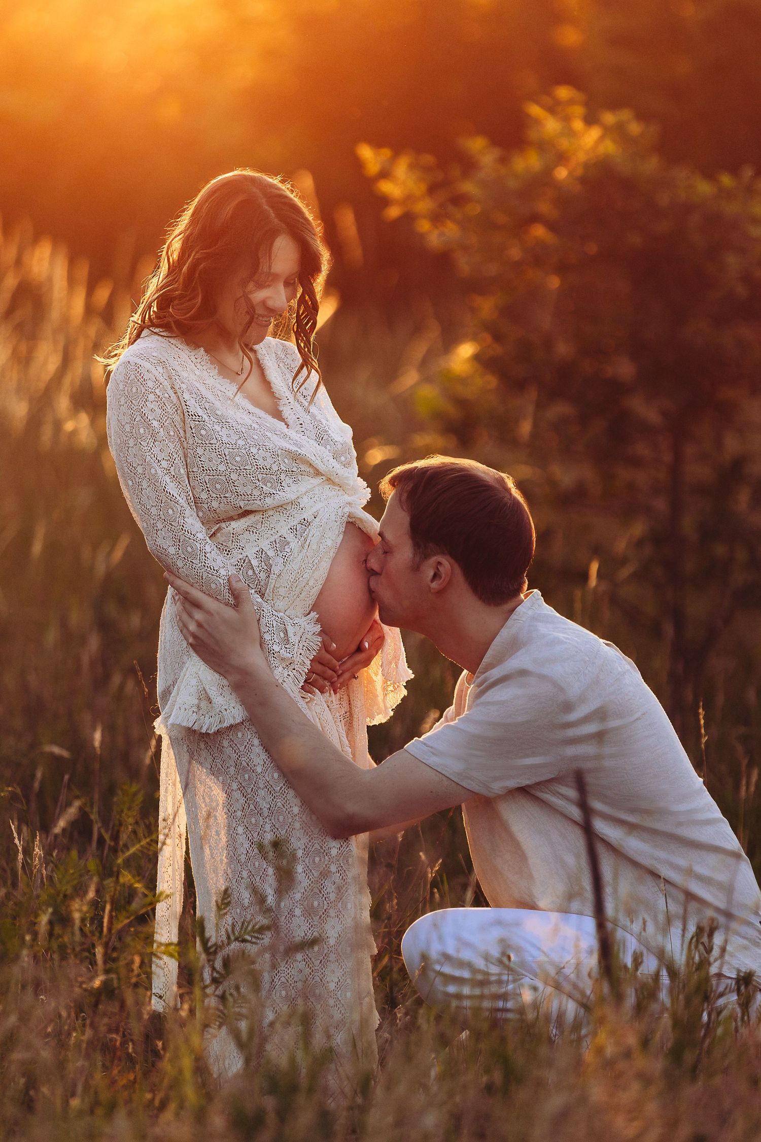 Intimate maternity session in tall grass during golden hour sunset.
