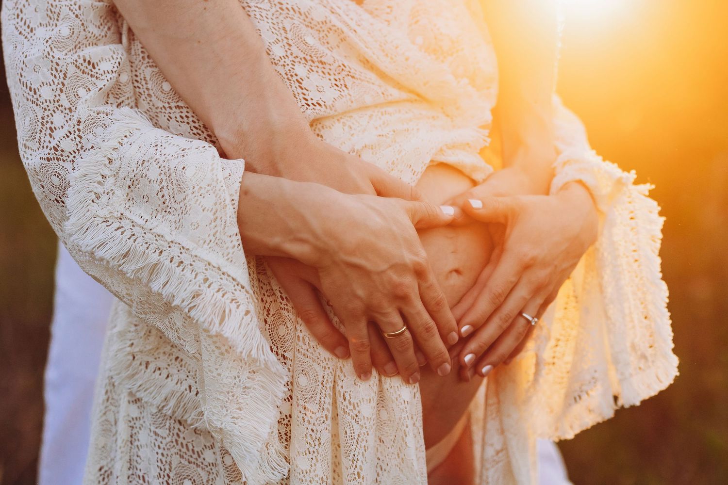 Close up of hands holding white lace dress fabric in golden sunlight.