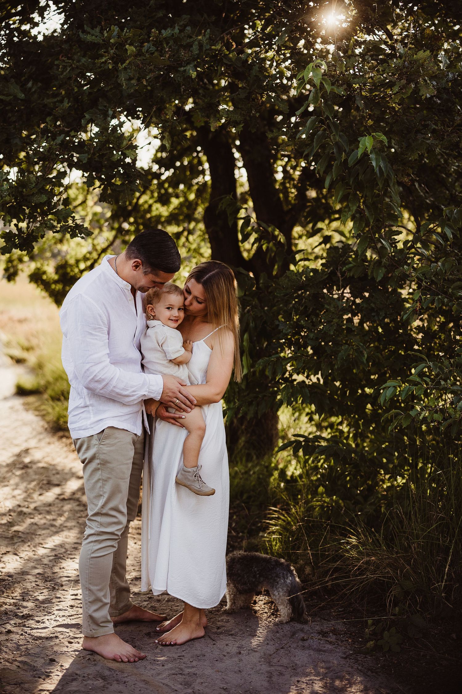 Family portrait session on a sandy path surrounded by lush greenery and sunlight.