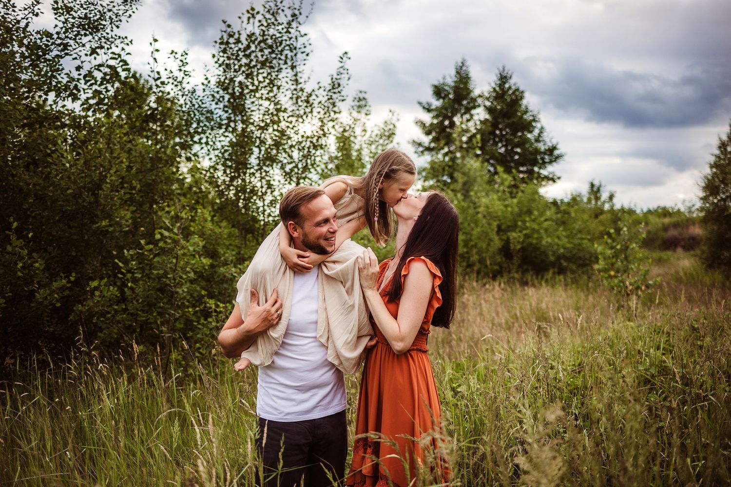 Beautiful outdoor family photoshoot in a meadow with dramatic cloudy sky.