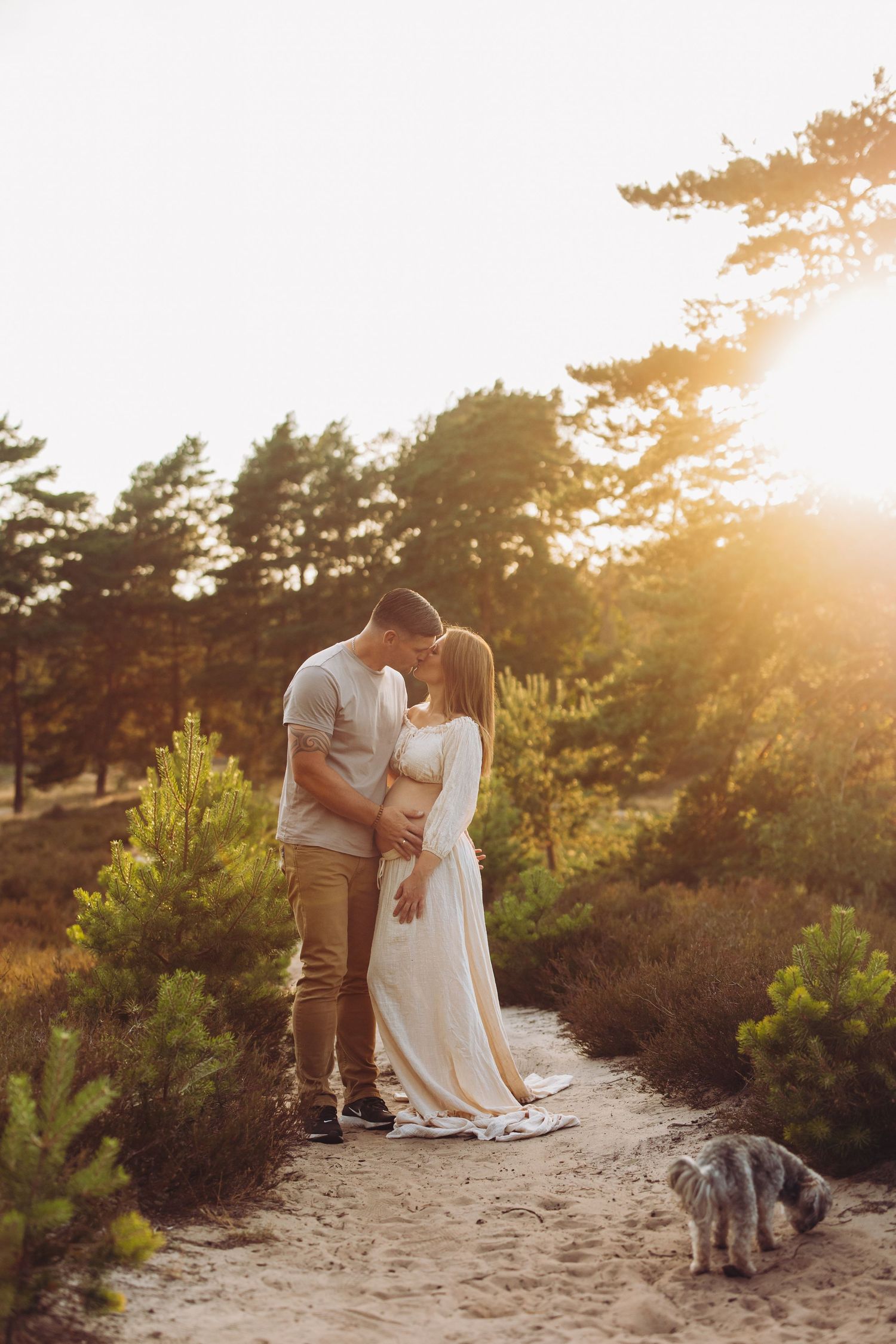 Sunset maternity photography session on sandy path with pine trees in background.