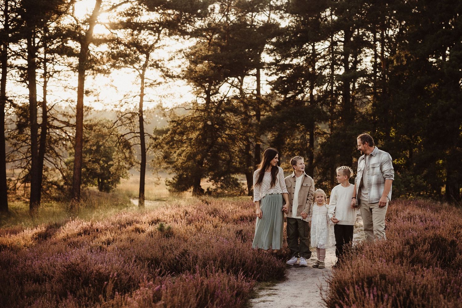 Family walking through field of purple heather during sunset photo session.
