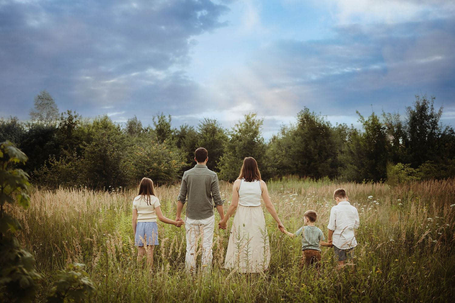 Family holding hands while walking through tall grass field at sunset.