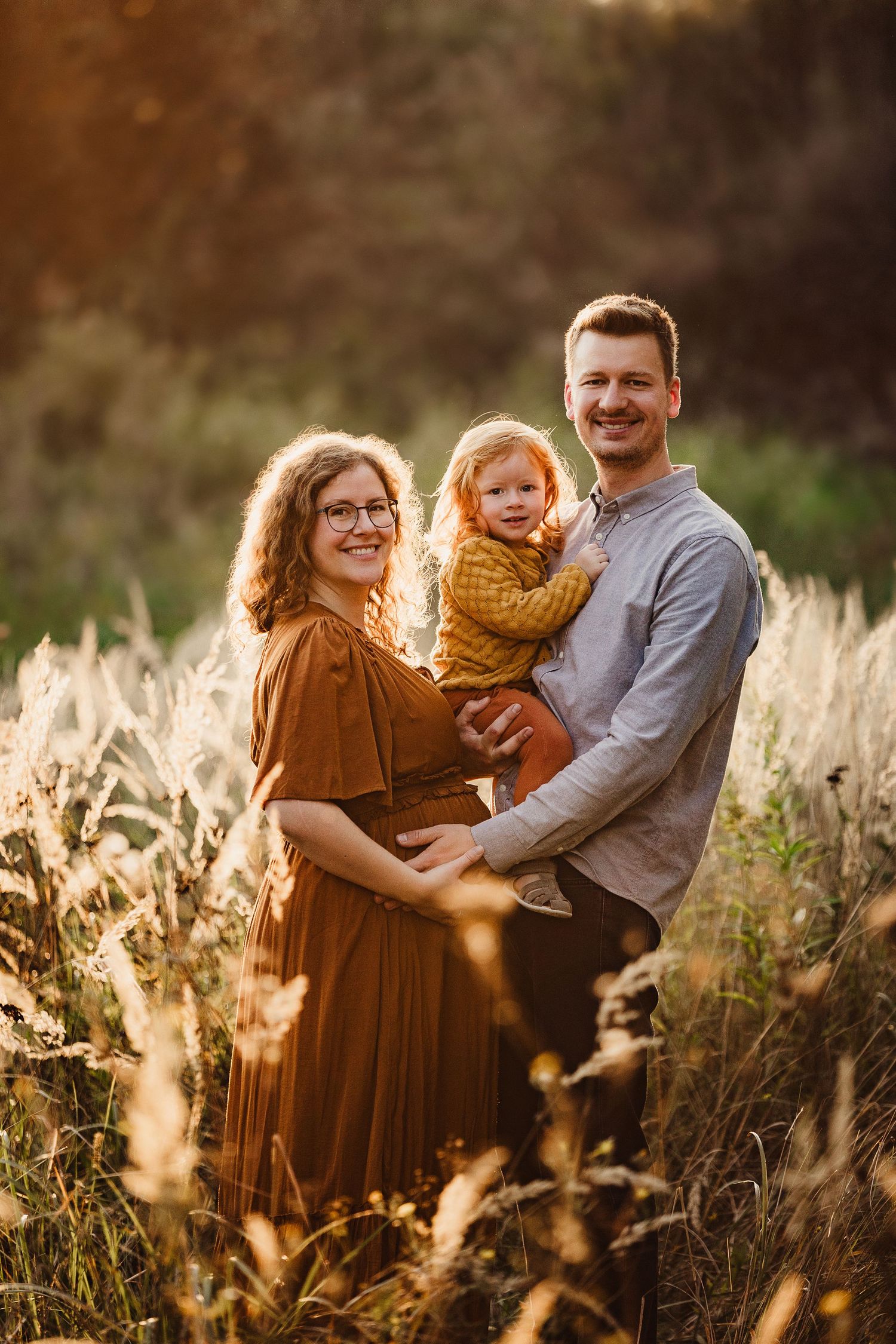 Family photo session in golden sunlit field with tall grass at sunset.