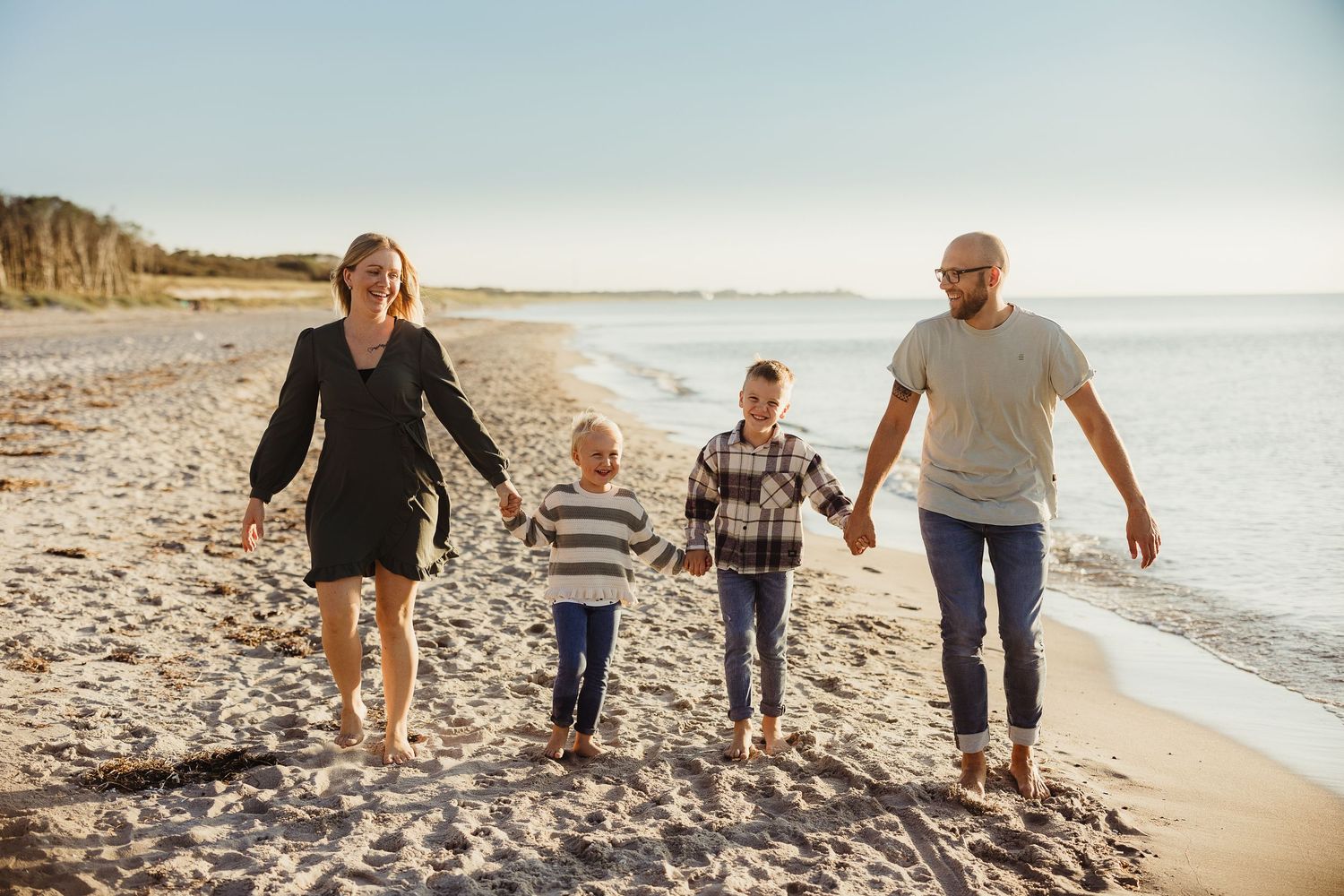 Family walking together holding hands along a scenic beach at sunset.