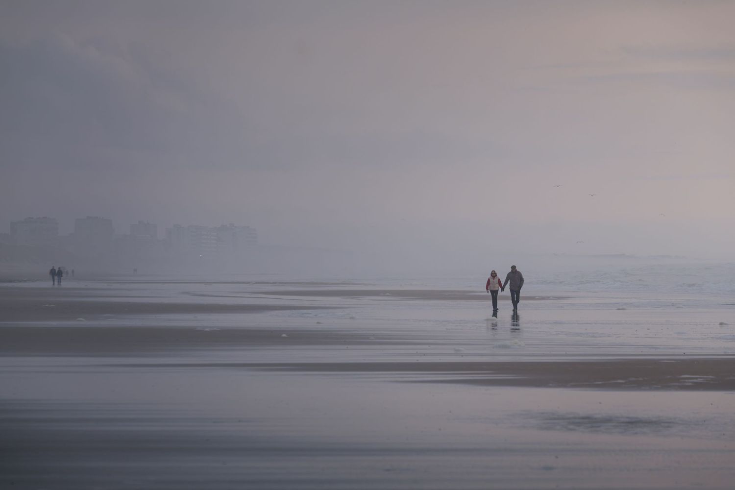 Photographie minimaliste et onirique d'un couple marchant sur une plage brumeuse, tourisme de ressourcement sur la Côte d'Opale.