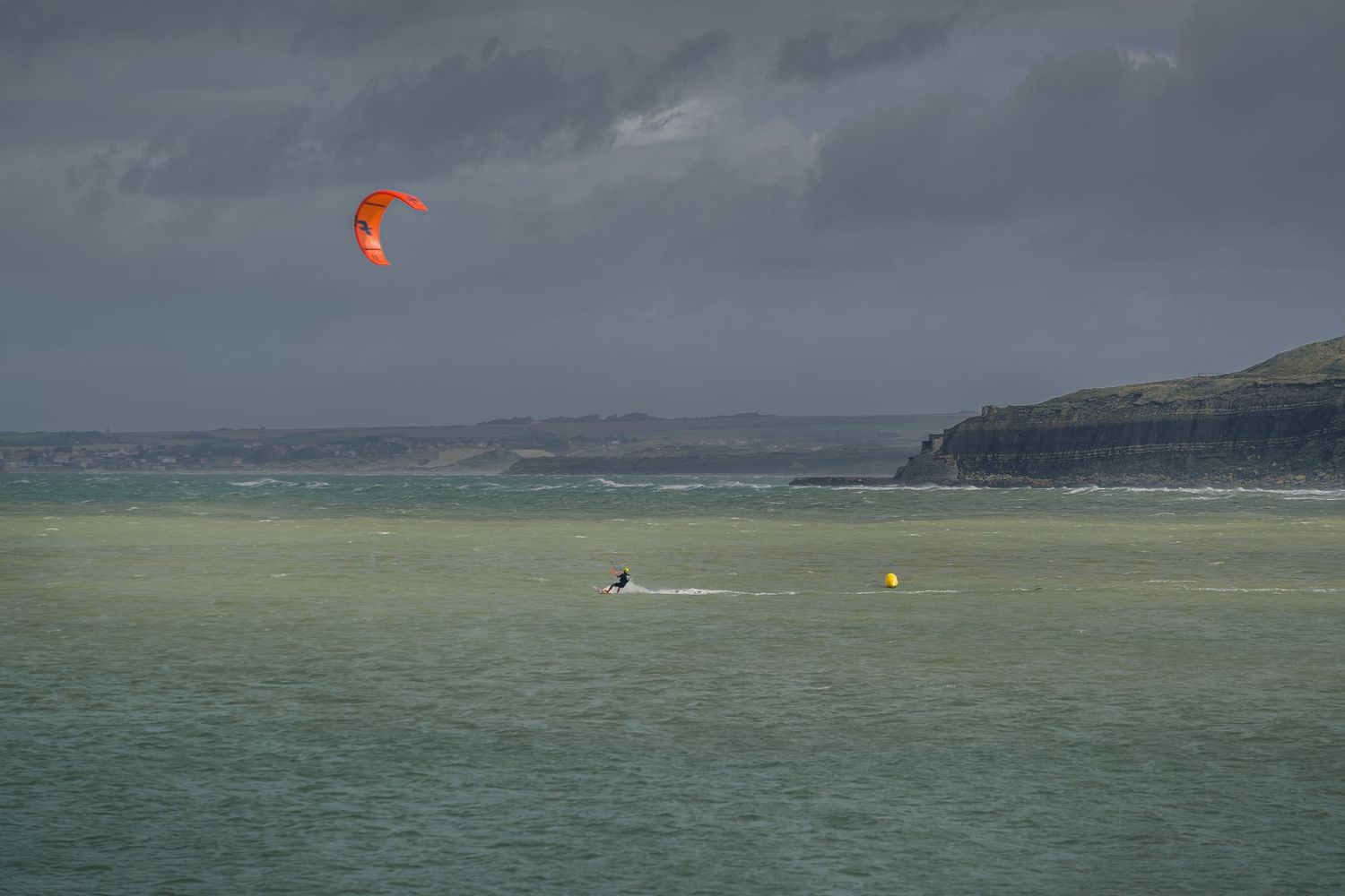 un jour de tempête avec des rayons de soleil, un sportif fait du kitesurf  à Boulogne sur Mer