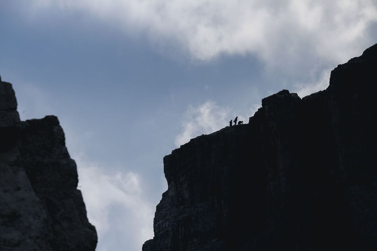 Alpiniste atteignant le sommet d'une tour rocheuse aux Cinque Torri dans les Dolomites, Italie, sous un ciel nuageux.