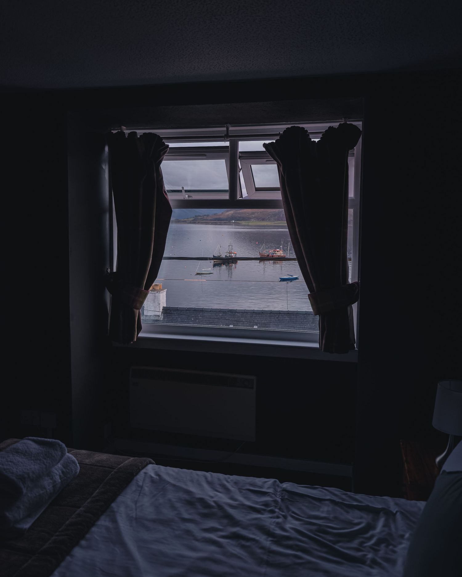 Vue depuis une fenêtre de chambre donnant sur le port d'Ullapool et les bateaux de pêche.