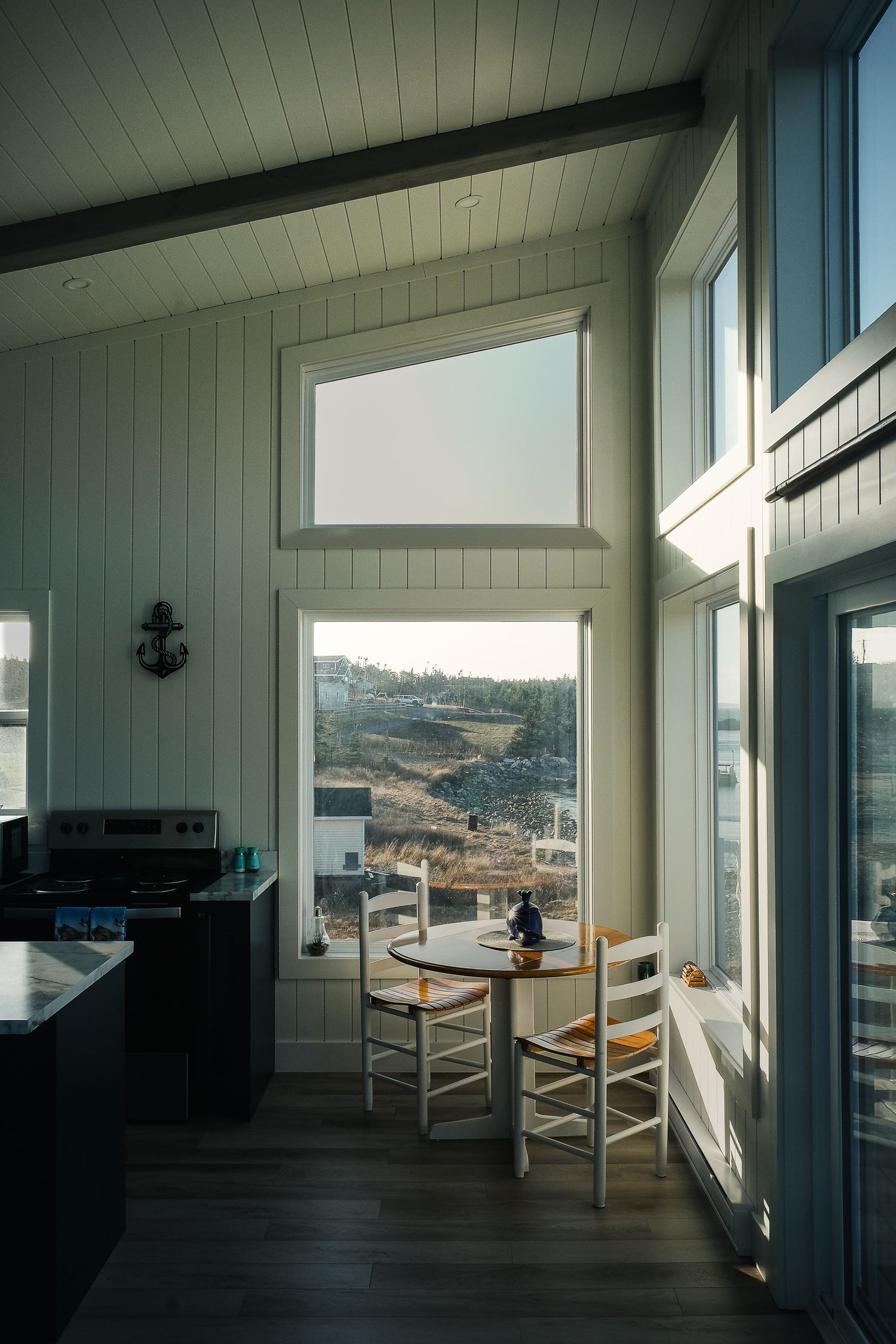 Coin repas lumineux avec vue panoramique sur la côte et le village depuis l'intérieur d'un logement typique à Dildo, Terre-Neuve.