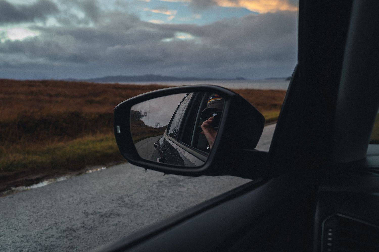 Reflet de la route sinueuse des Highlands dans le rétroviseur d'une voiture, symbole du voyage itinérant en Écosse.