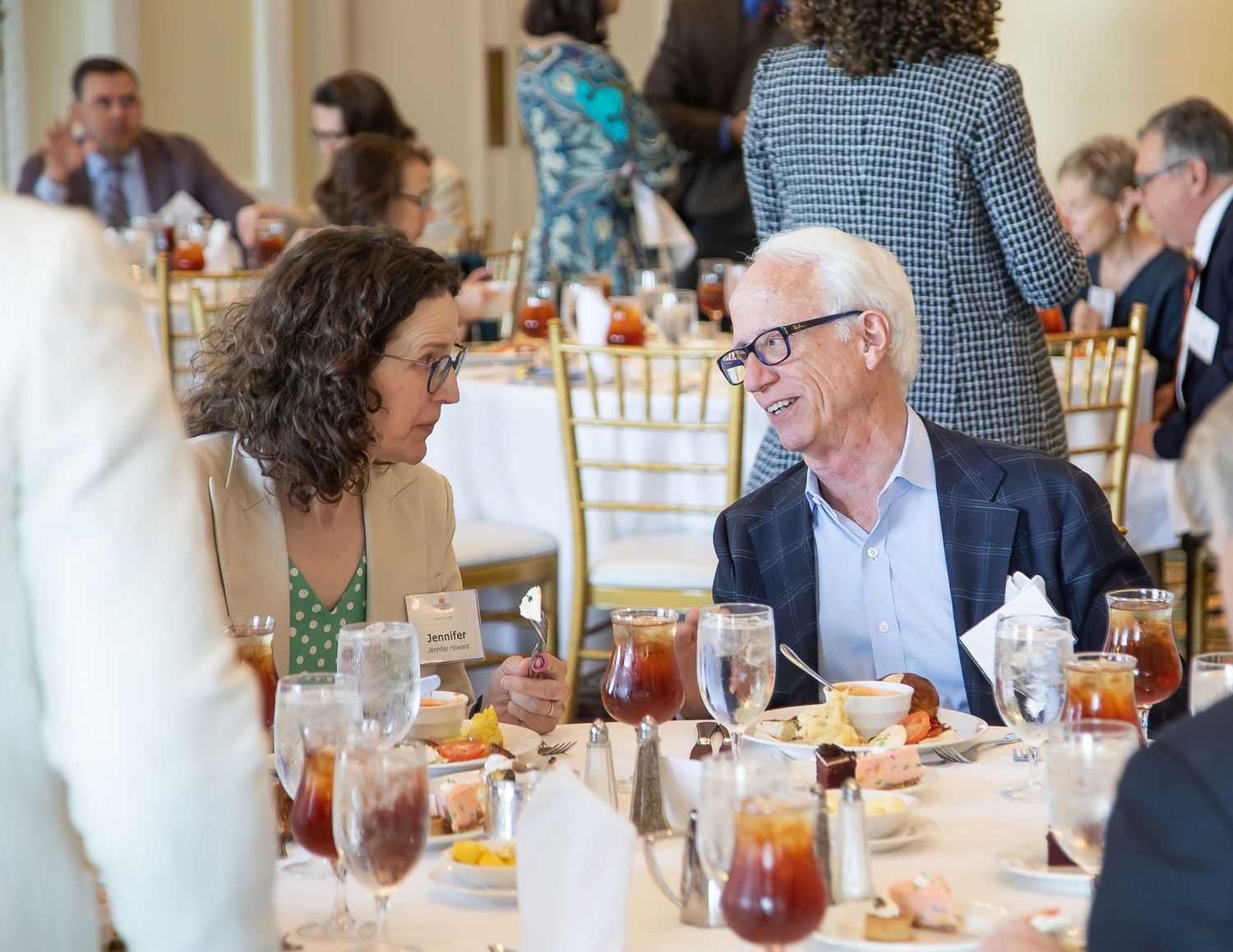 Two professionals engage in conversation at an elegant banquet dinner event with gold chairs and formal table settings.