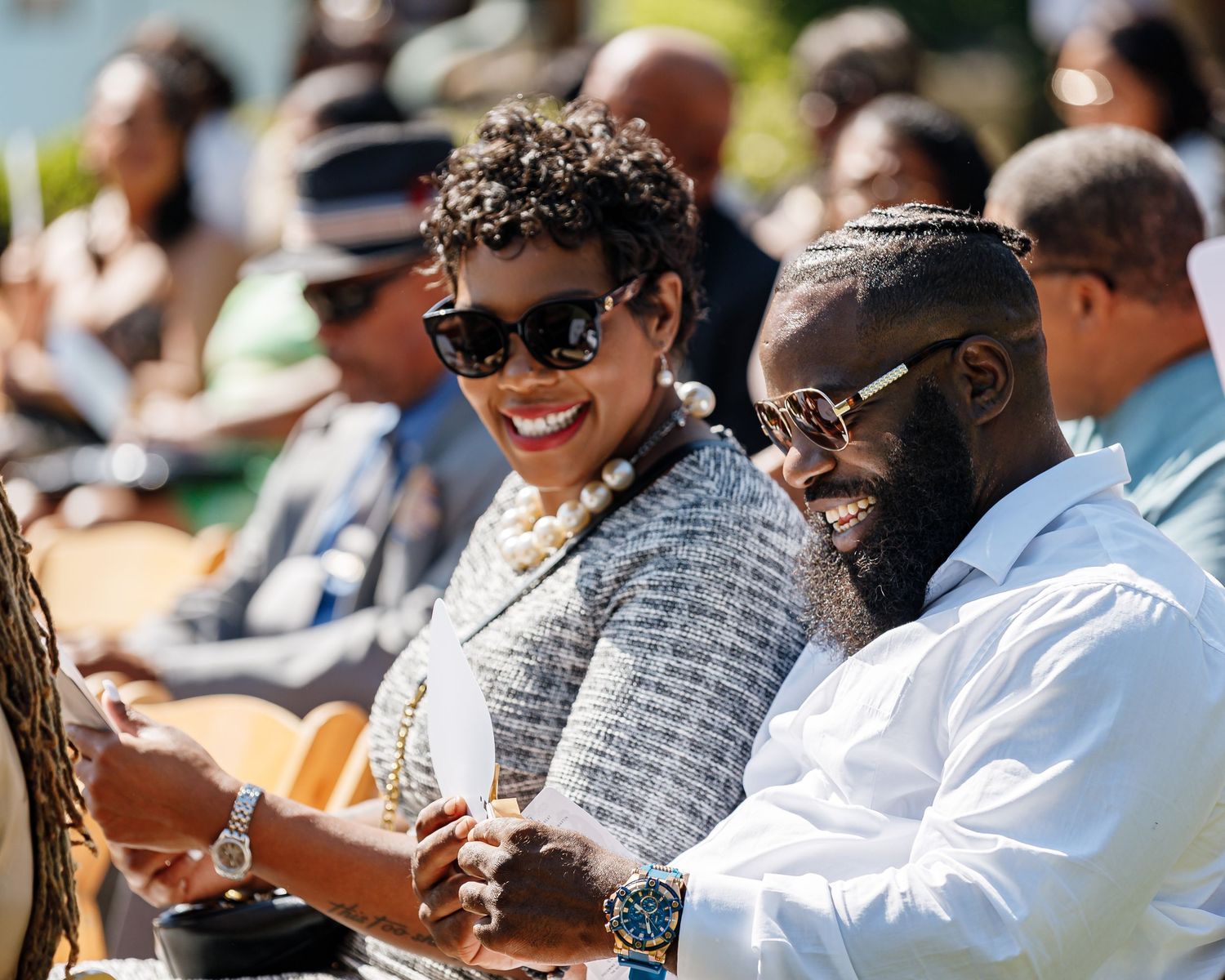 Outdoor wedding guests enjoying a sunny celebration while seated in rows.