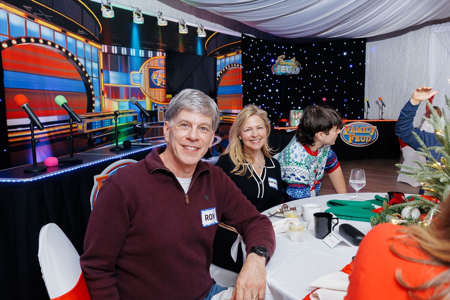 Smiling couple seated at a decorated banquet table at a colorful game show themed event.