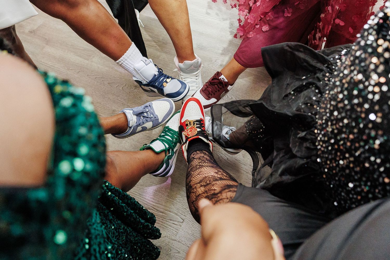 Group of people in formal wear showing off colorful sneakers in a circle, mixing elegant dresses with casual footwear.