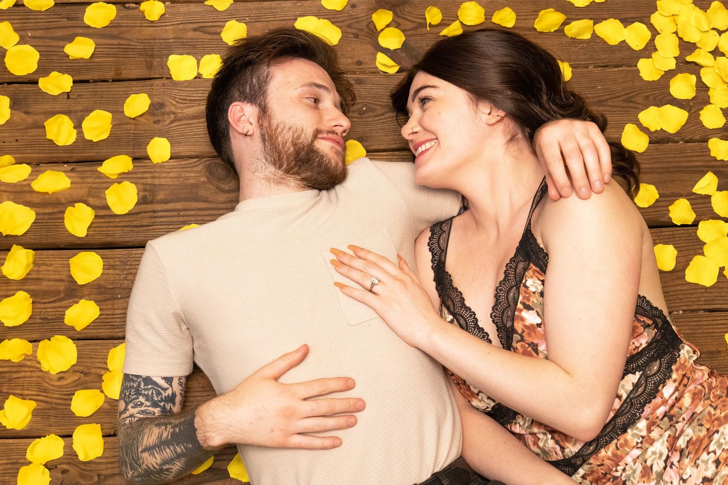 A couple lying on wooden floor surrounded by yellow fairy lights.