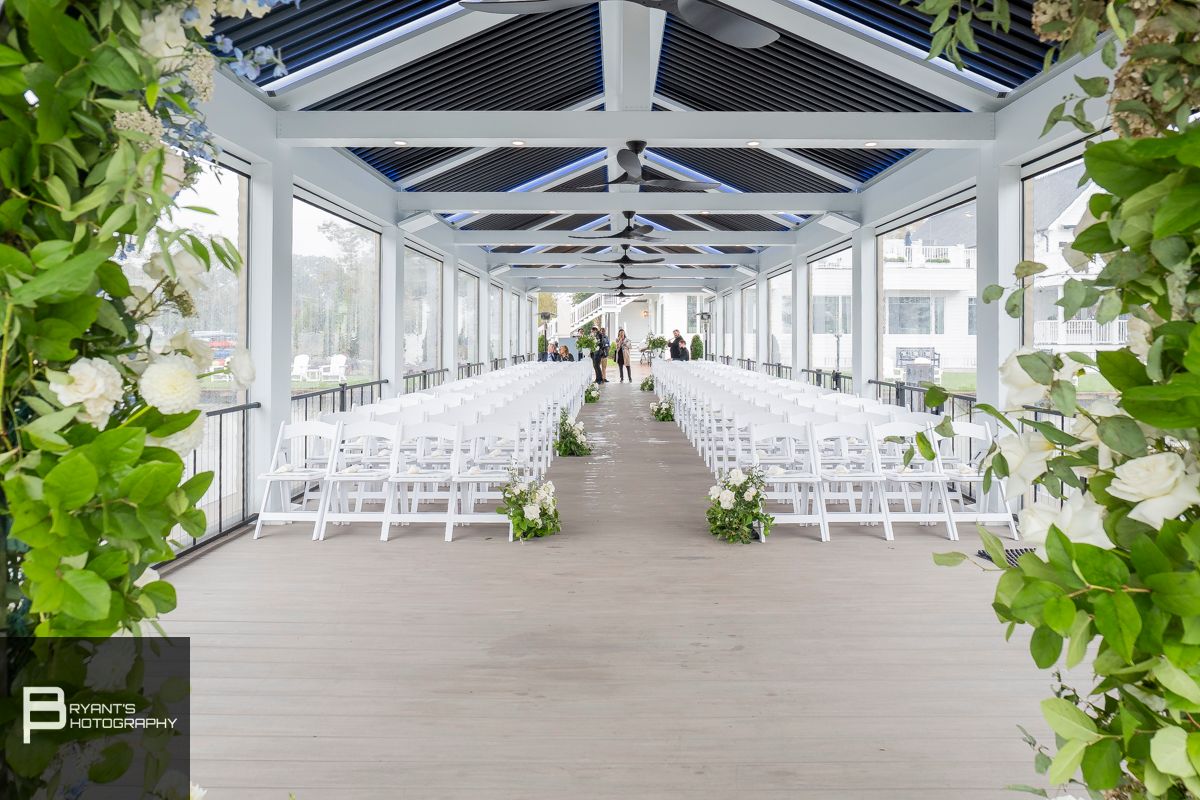 White indoor wedding ceremony venue with rows of chairs and floral decorations.
