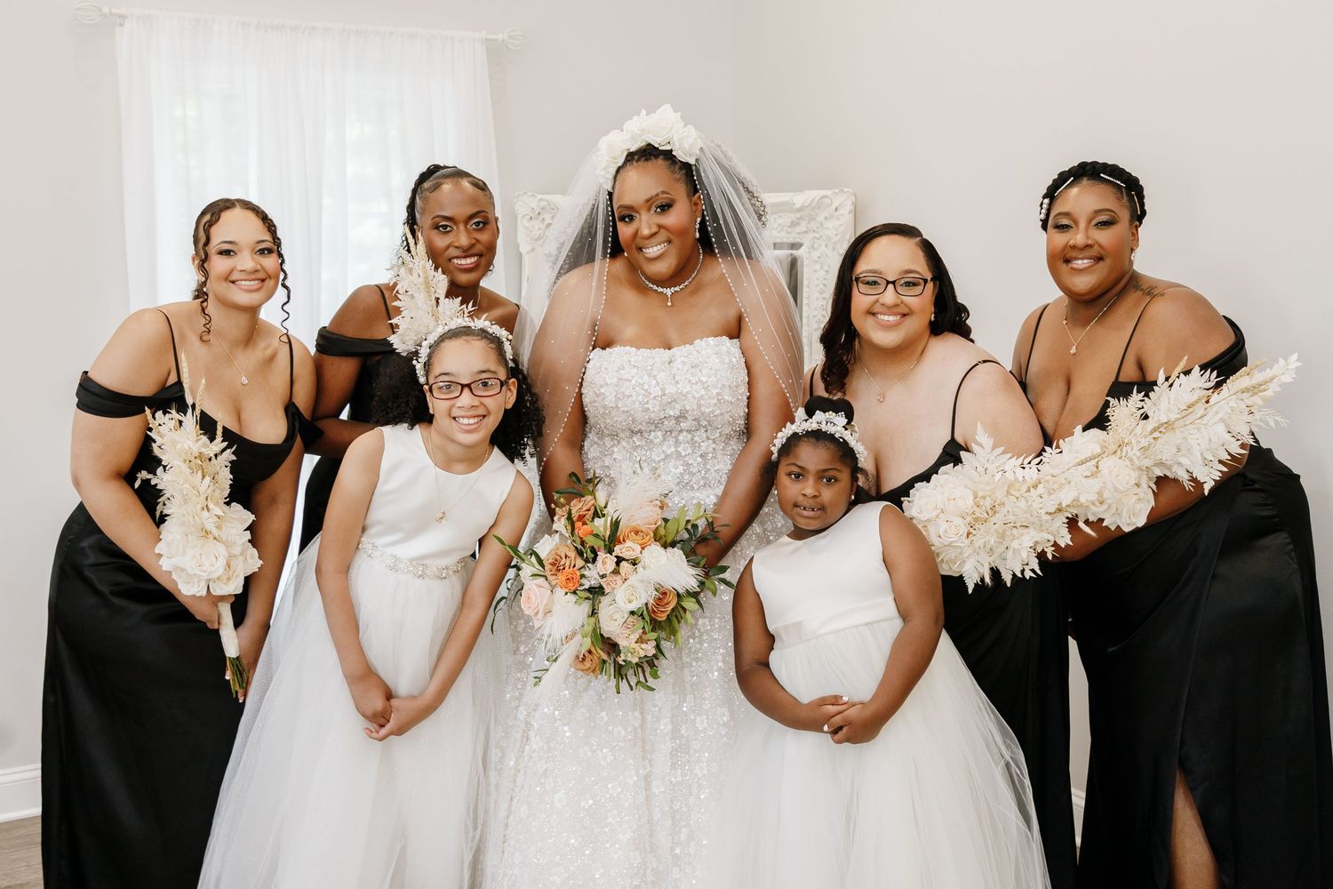 Wedding party members in black dresses posing together in a bright indoor setting.