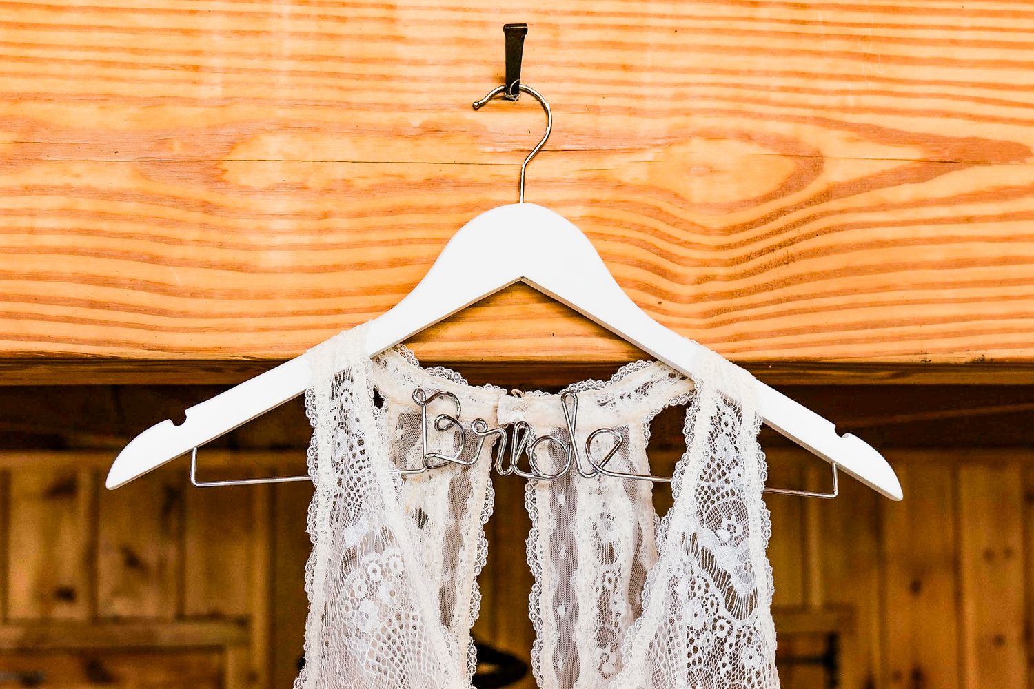 White lace wedding dresses hanging on wooden hangers against rustic wood paneling.