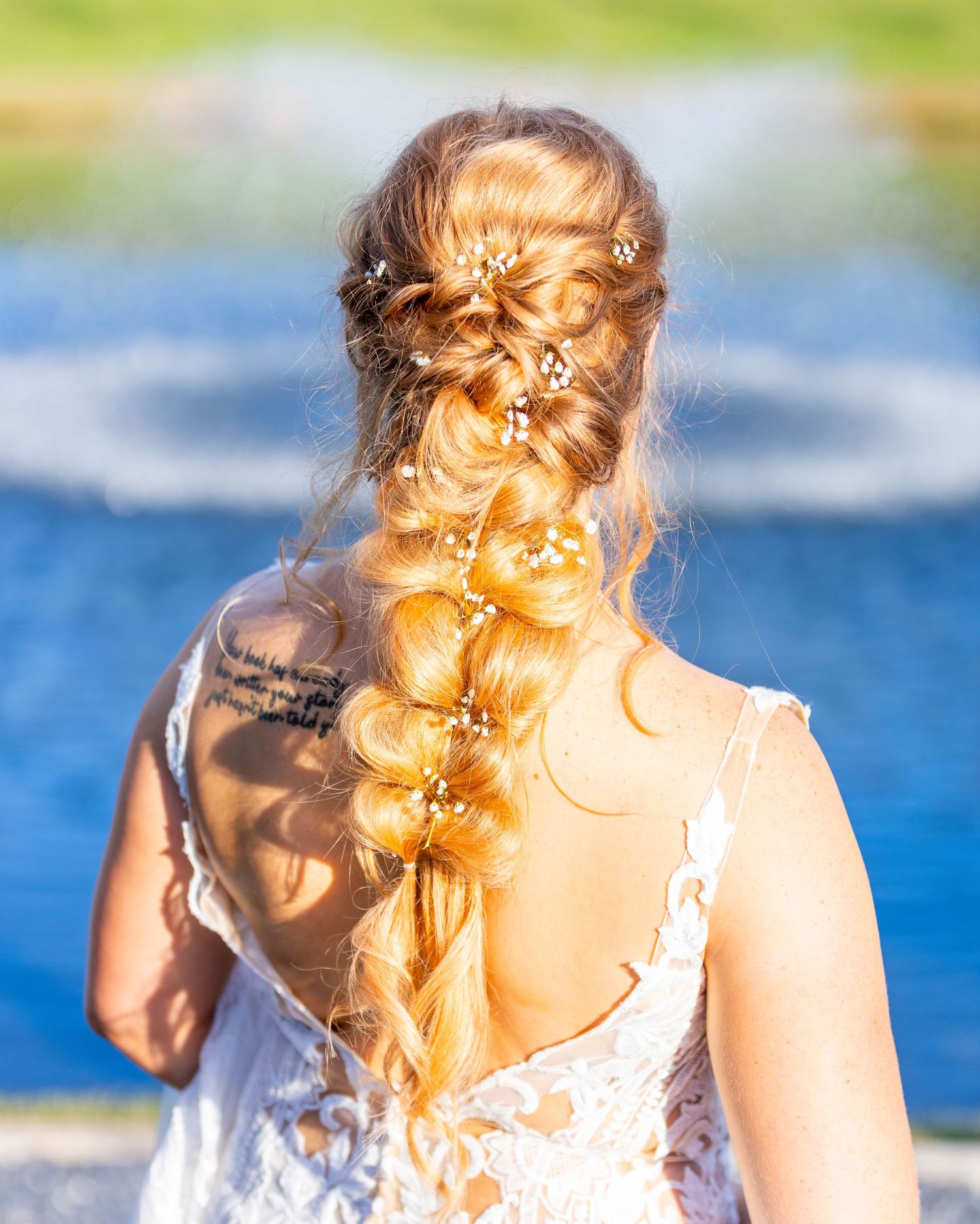 Intricate braided hairstyle with floral accessories photographed against a blue water background.