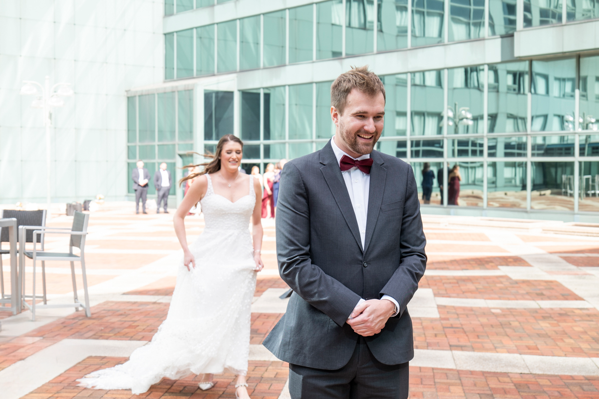 Wedding couple shares a joyful moment together on a sunny day outside a modern glass building.