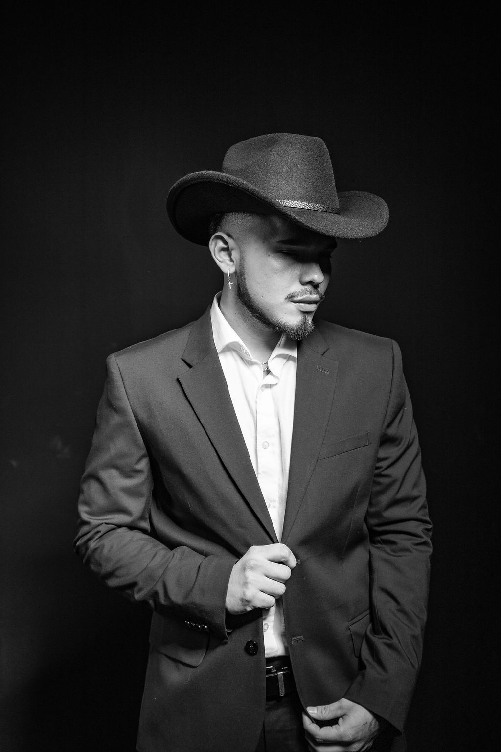 Black and white portrait of a man in a suit and cowboy hat posing against a dark background.