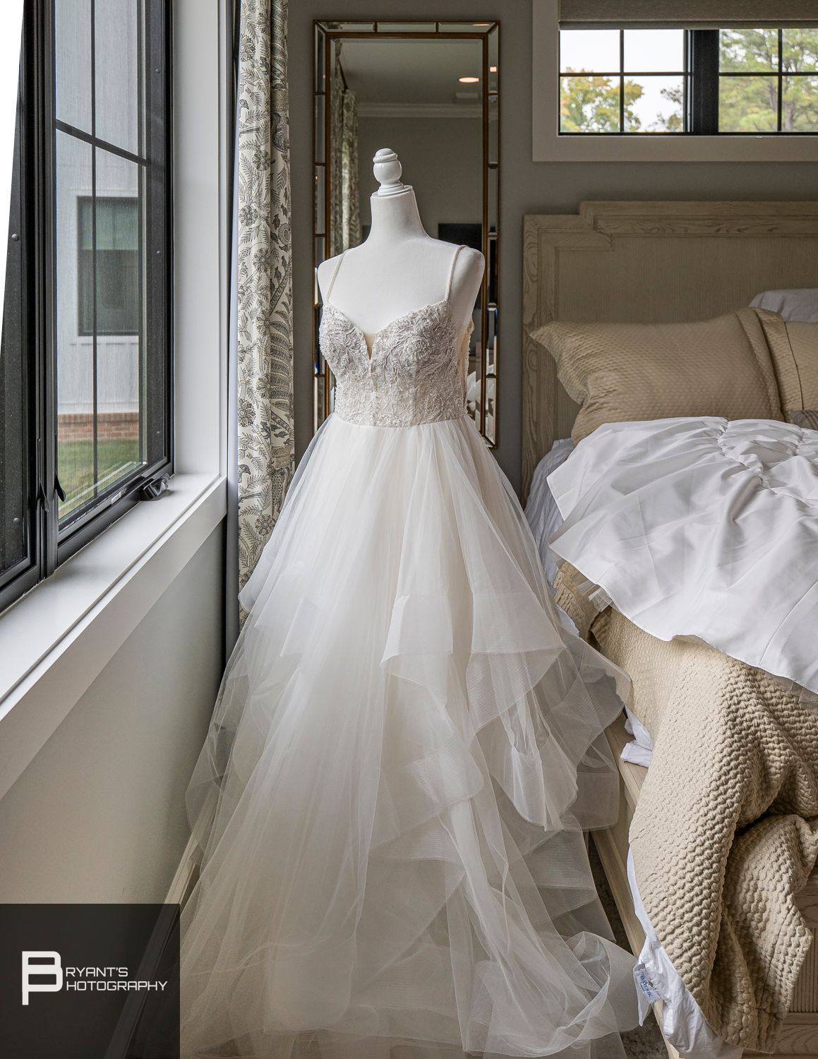 Ethereal white wedding dress with layered tulle skirt displayed on mannequin by window.