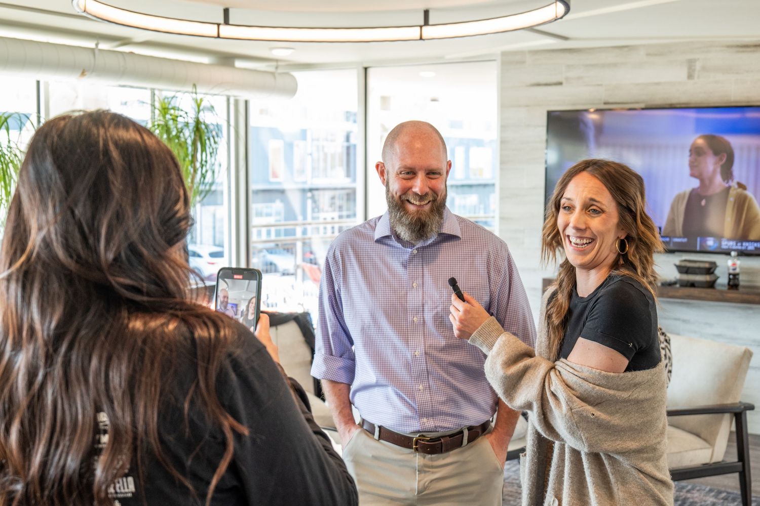 Three professionals networking in a modern office, smiling and conversing near a large display screen.