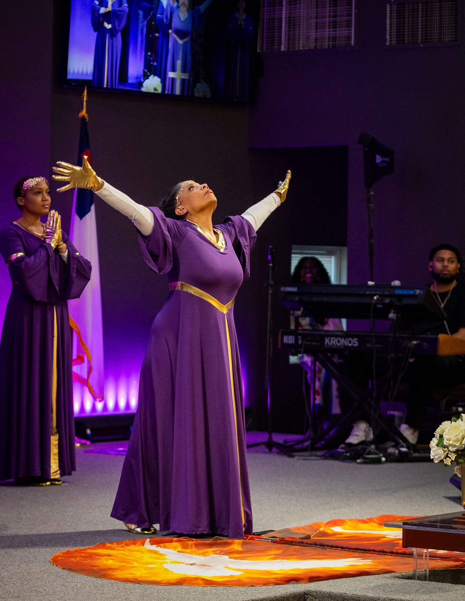 Woman in purple liturgical dance dress with arms raised during a church worship performance.