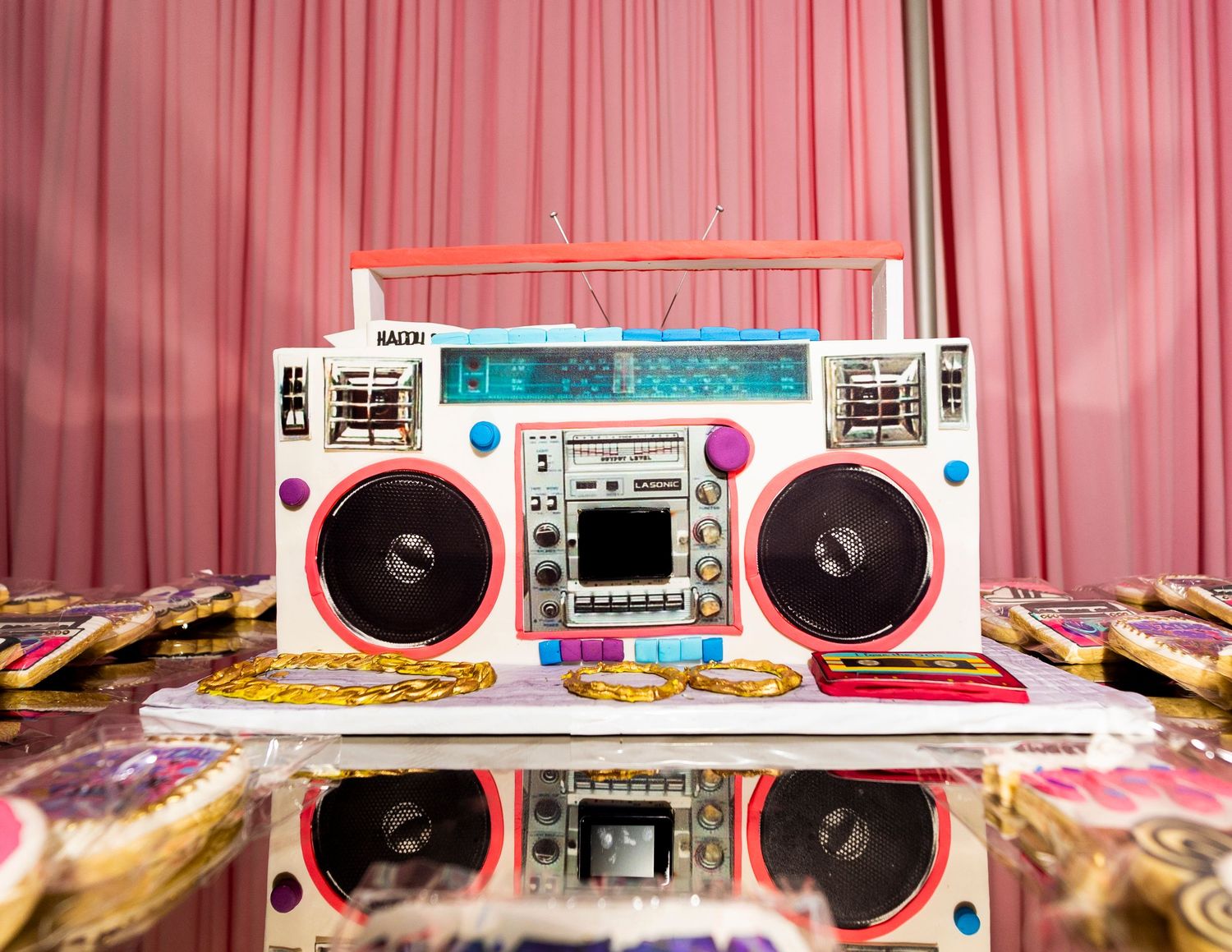 Colorful retro boombox with pink speakers on a reflective surface against pink curtains.
