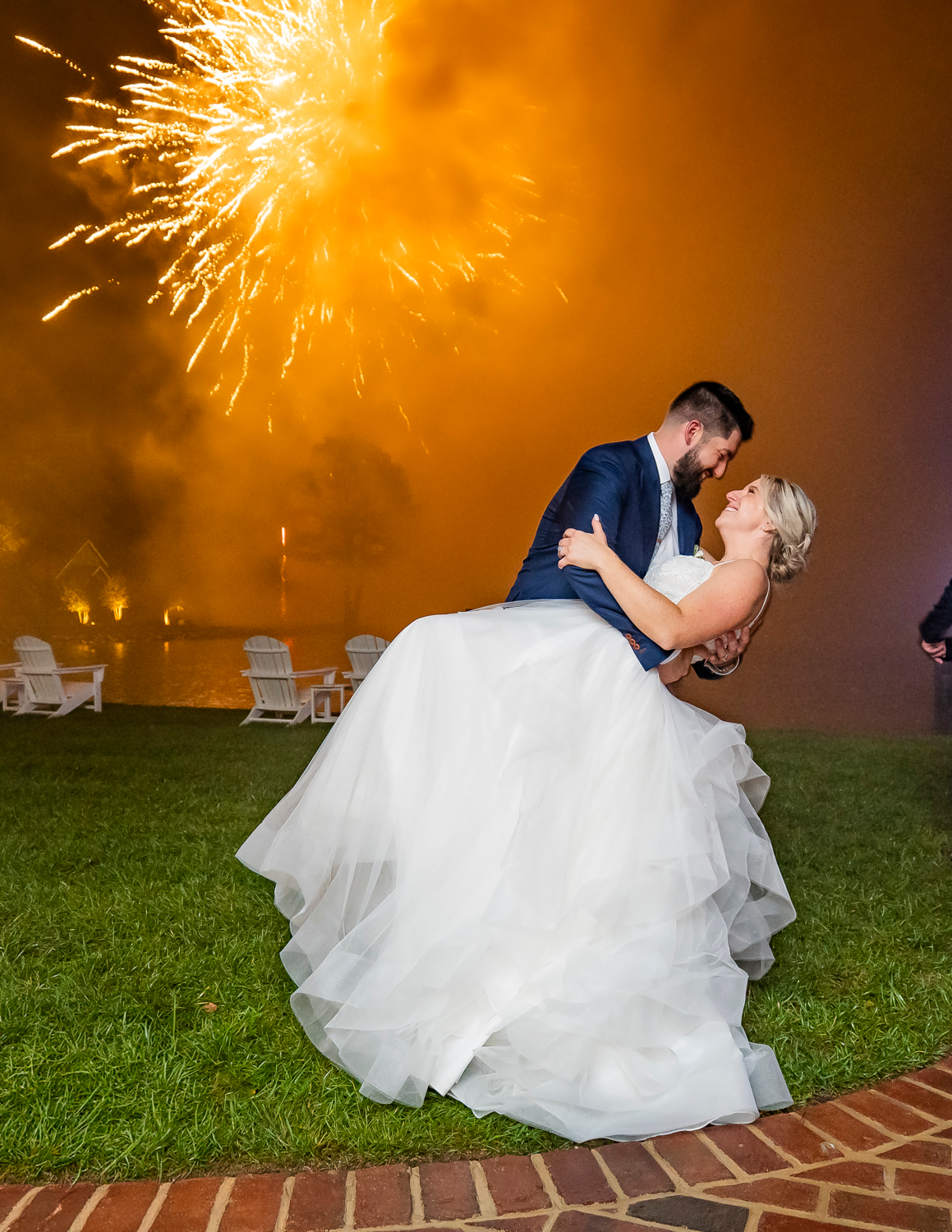 Wedding couple shares romantic dip kiss under orange fireworks display.