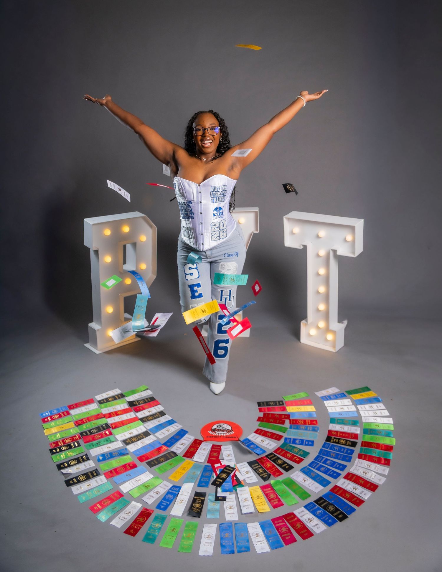 Woman in decorated outfit jumping joyfully between lit marquee letters R and T, surrounded by colorful tickets on floor.