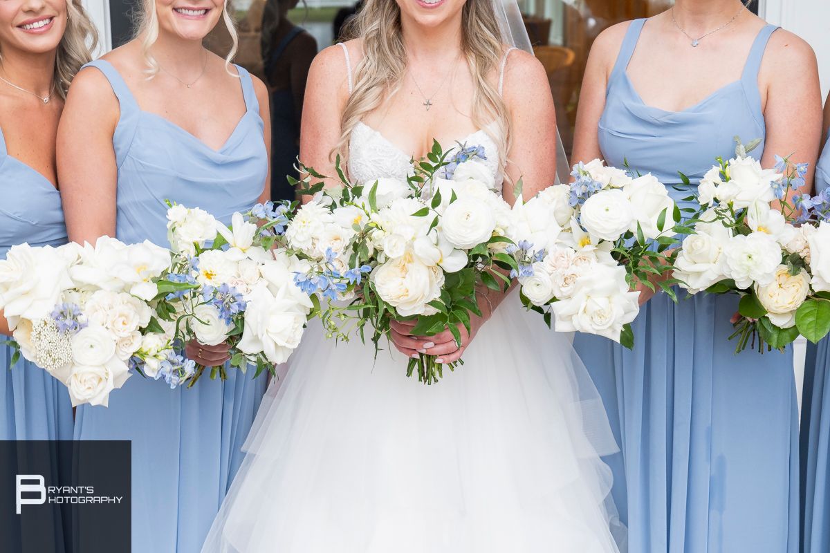 Bridesmaids in light blue dresses holding white floral bouquets.
