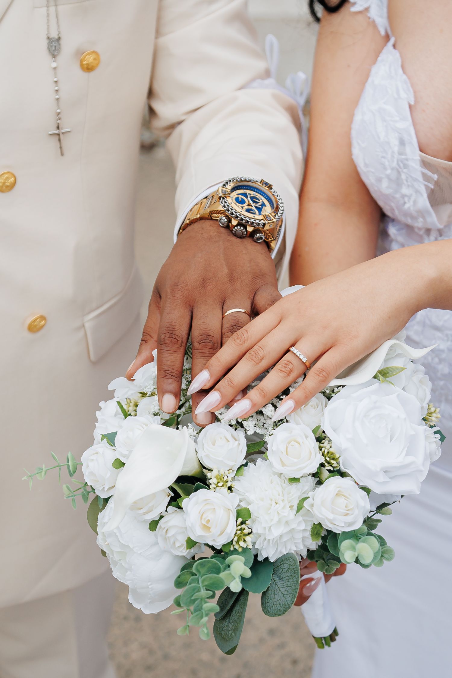 Close-up of white rose bouquet and wedding rings against light background.