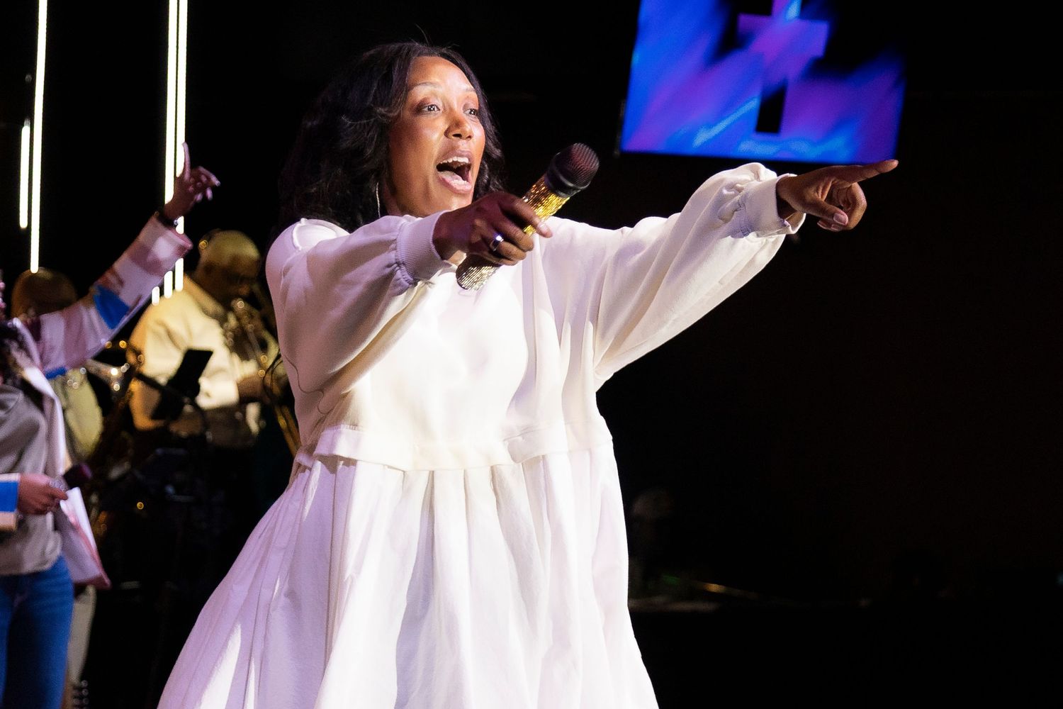 Woman in white robe singing passionately on stage, pointing outward during a gospel choir performance.