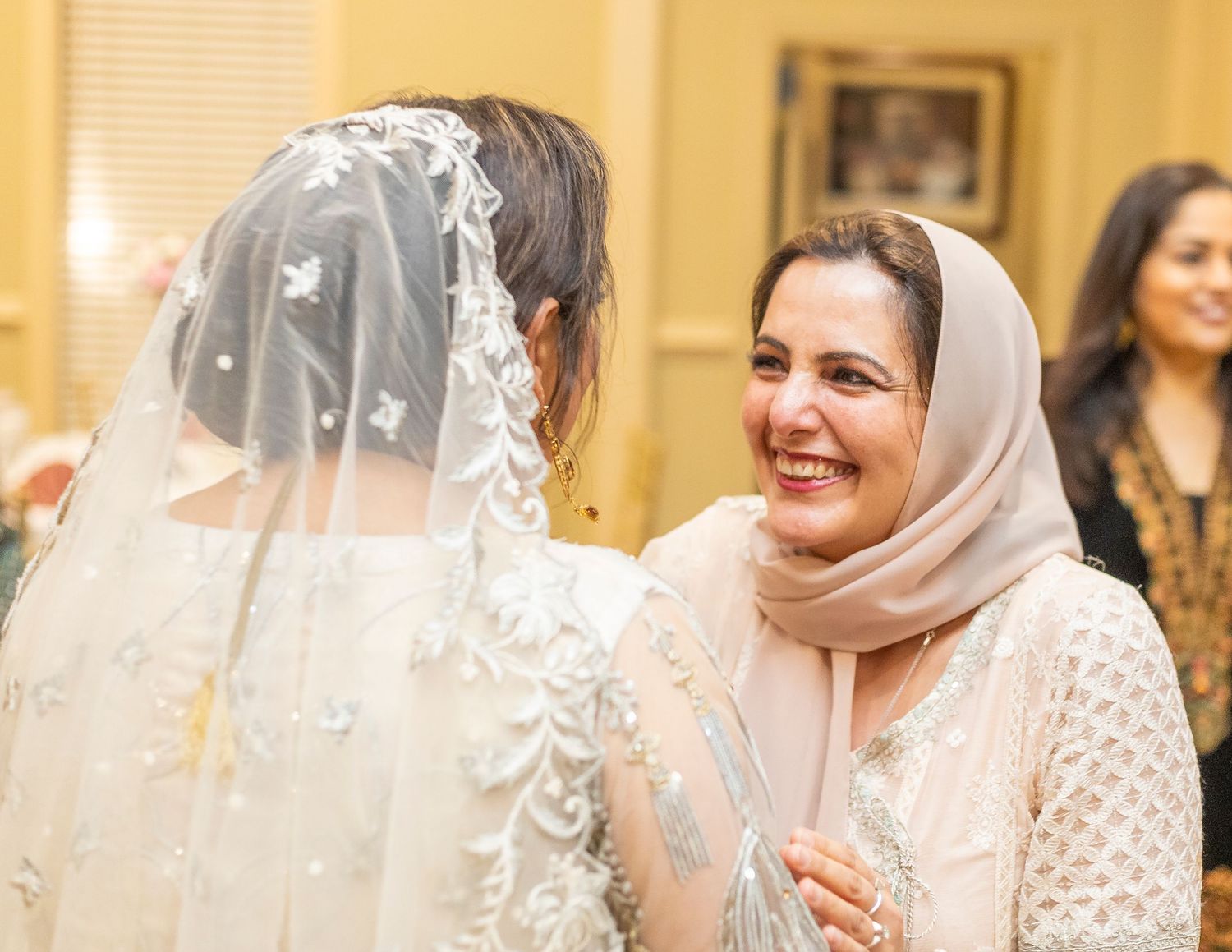 Two women in elegant South Asian attire share a joyful moment at a wedding celebration.