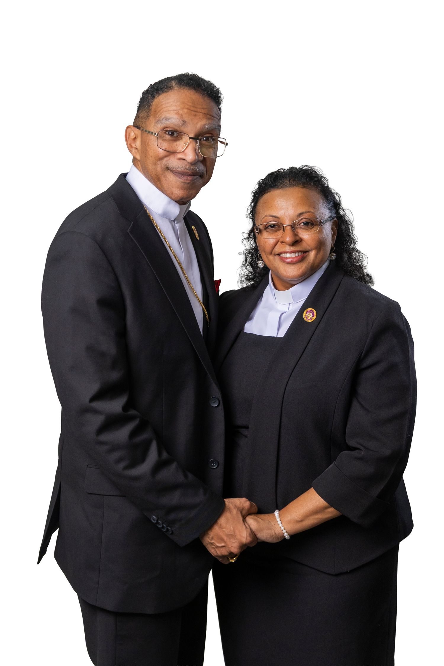 Two professionally dressed individuals in black suits smiling and holding hands against a white background.