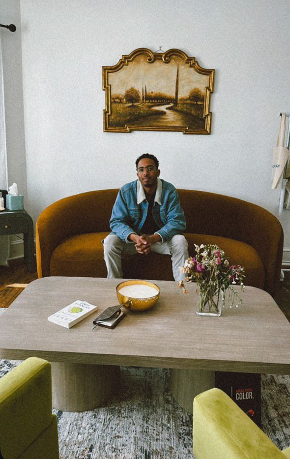 Person relaxing on vintage brown couch with decorative artwork on wall.