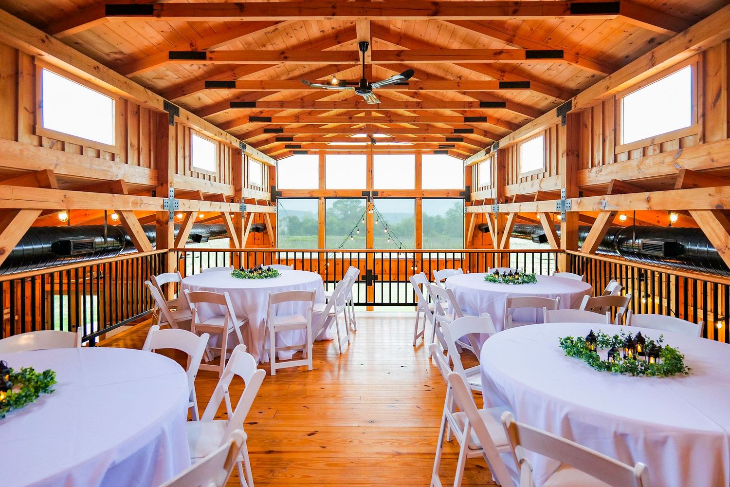 Rustic wooden event venue interior with exposed beams, ceiling fans and white reception tables.