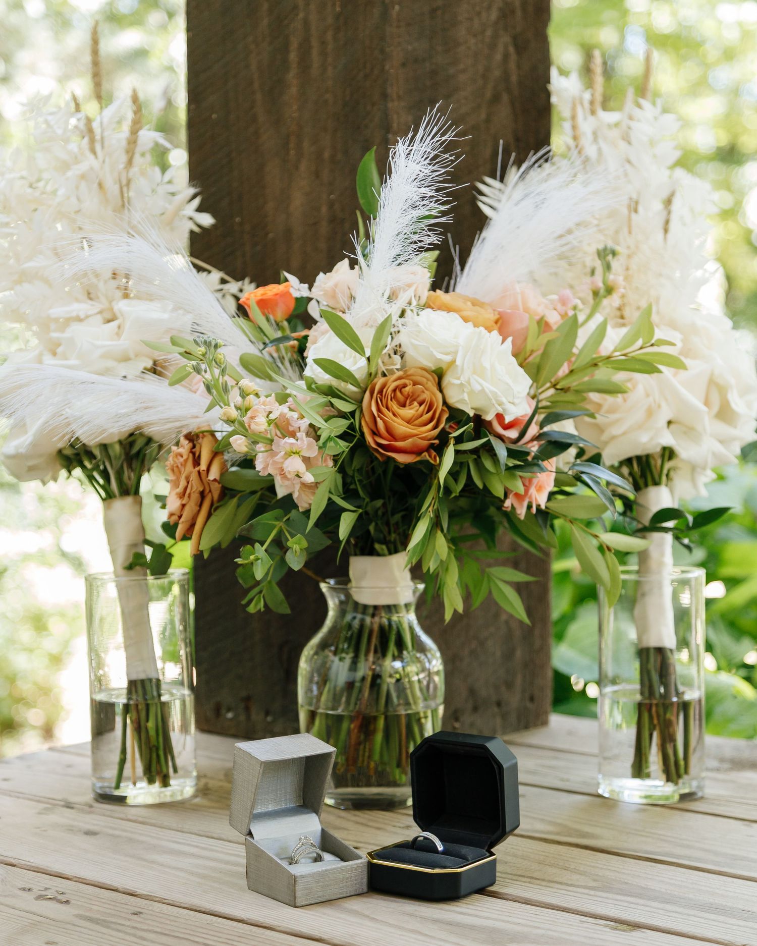 Elegant floral centerpieces with white feathers and roses arranged in glass vases on a wooden surface.