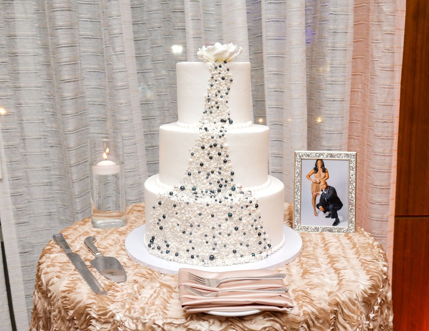 Elegant white wedding cake with cascading sparkly details on a mirrored display stand.